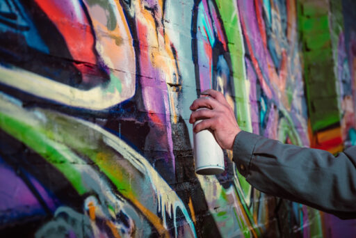 Ausgeschnittene Ansicht eines Straßenkünstlers, der nachts Graffiti mit Sprühfarbe an die Wand malt