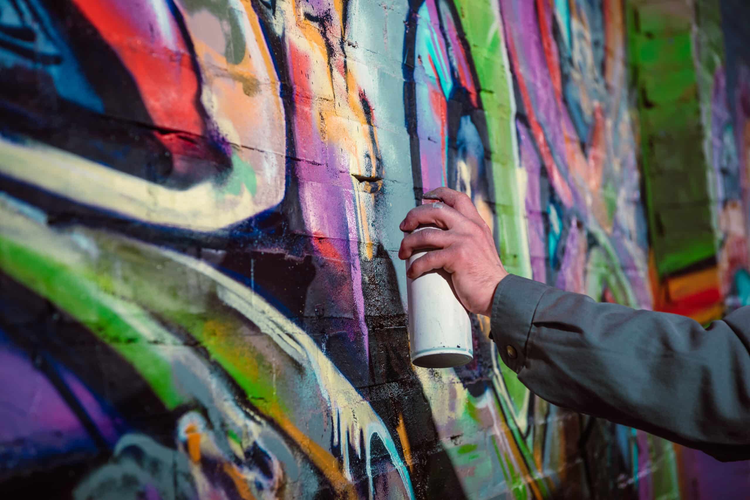 Ausgeschnittene Ansicht eines Straßenkünstlers, der nachts Graffiti mit Sprühfarbe an die Wand malt