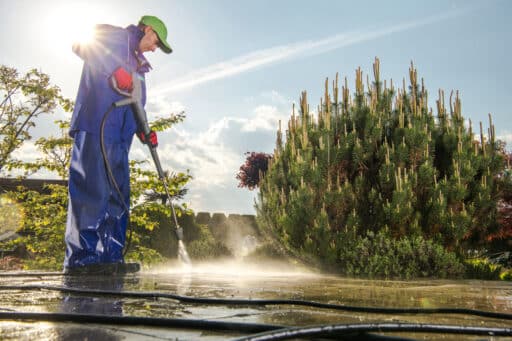 Mann mit Hochdruckreiniger reinigt Terrassenfläche im Garten